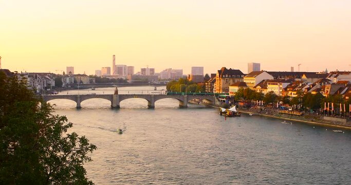 Panorama of Basel city, sunset light, water traffic on rhine river, city traffic on the bridge, summer in Switzerland.