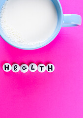 milk in blue cup and inscription HEALTH made of white medical pills on a bright pink  background. healthy lifestyle concept