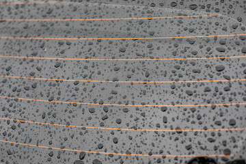 Drops of water on the rear window of the car, orange heating threads. Black tinted car glass with a heating element wet in the rain