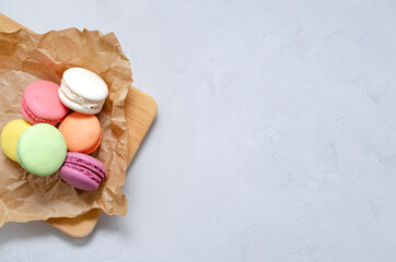 many multicolored crunchy delicious macarons on craft paper for baking on gray concrete background. morning coffee concept. sweets and desserts. with copy space.