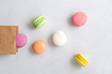 multicolored mouth-watering crunchy macaroons poured out of a paper craft bag against a light gray...