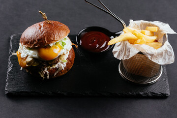 Burger with beef Patty and egg, French fries and sauce on a blac