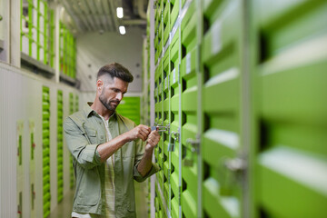 Waist up shot of handsome bearded man opening padlock on door of self storage unit , copy space