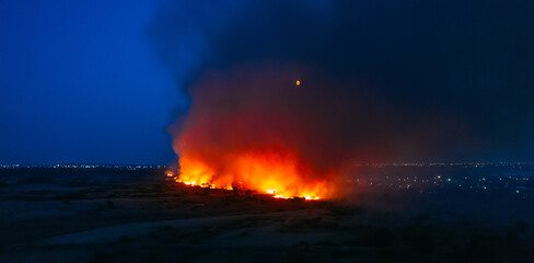 Flames of massive Forest Fire, aerial view at night. Nature wildfire in dry season. Burning trees and meadows.