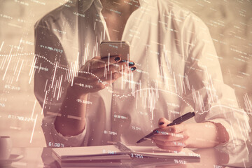 Double exposure of financial graph sketch hologram and woman holding and using a mobile device. Stock exchange concept.