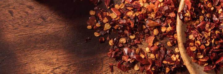 Crushed red pepper flakes on a plate spilled over wooden surface. Ideal for food recipe or restaurant menu signs