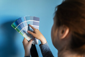 Back view of unknown caucasian woman holding color palette at home against a wall choosing paint...