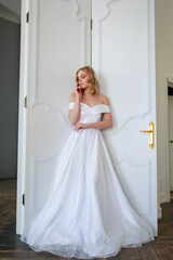 A bride in a chic wedding dress stands near the door and looks to the side