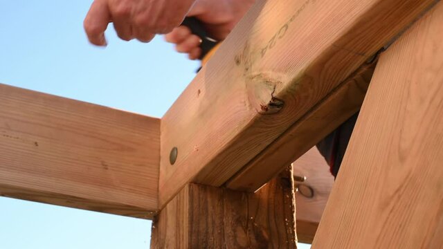 Male hands using impact driver to build wooden gazebo