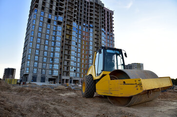 Vibro Roller Soil Compactor leveling ground at construction site. Vibration single-cylinder road roller on construction road. Road work for new asphalt laying. Tower cranes build high-rise buildings