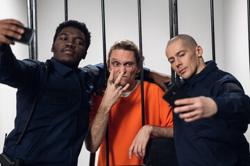 Warders in full gear take selfies on a smartphone with a dangerous criminal behind bars. Black guy...