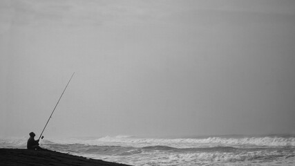 Silhouette of man fishing by the sea. Sitting alone holding the long fishing rod.