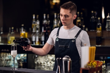 a young male bartender fills a glass of champagne at the bar in a nightclub.
