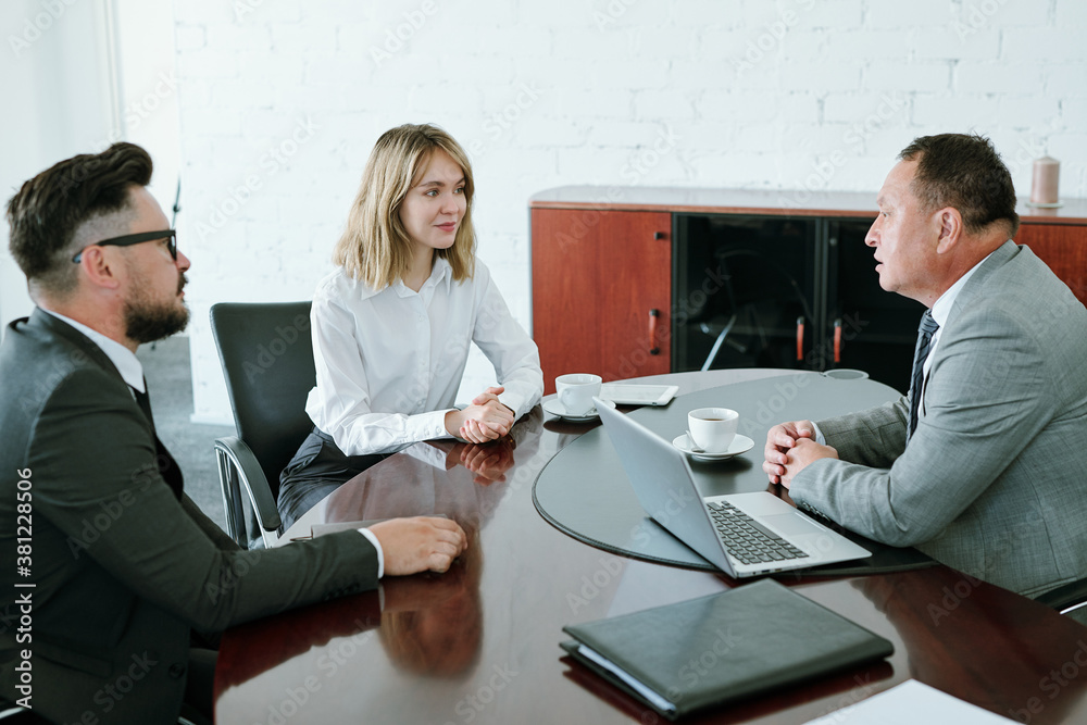Poster subordinates in formalwear sitting by table in boardroom in front of director