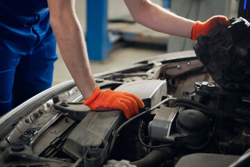 A repairman in gloves inspects a faulty car engine. Close-up
