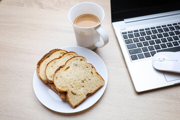 Slices of bread with a cup of coffee and laptop on wooden table 