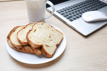 Close view of slices of bread and a cup of coffee with the laptop on wooden table 