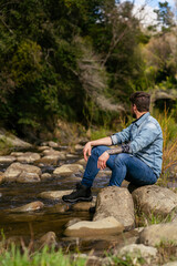 Young man admiring the natural environment that surrounds him while sitting at edge of river.