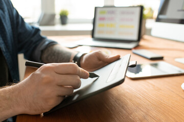 Hands of young creative designer with stylus over tablet drawing sketch of logo