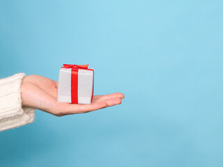 hand holding a gift box
woman's hand holding a gift box in the palm of the right on a blue background with a place for text on the left, close-up side view
