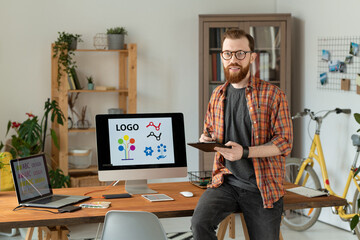 Cheerful freelance designer holding stylus over tablet while sitting on table
