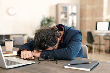 Young overworked businessman in formalwear napping in front of laptop