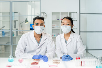 Two young intercultural clinicians in whitecoats, protective masks and gloves