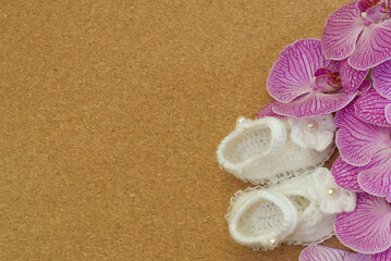 Fototapeta na wymiar purple and white orchid petals with small knitted shoes lie like postcard frame on brown textured background, copy space