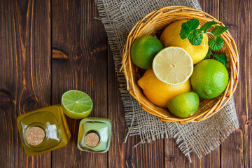 Limes with lemons, soft drinks, herbs in a wicker basket on wooden and piece of sack background,...