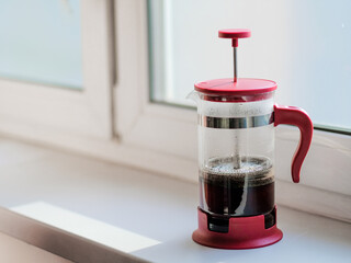 Glass Frenchpress on the windowsill in the rays of bright sunlight. The process of brewing ground...