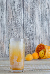 Scattered apricots from a wicker basket with juice side view on a wooden background