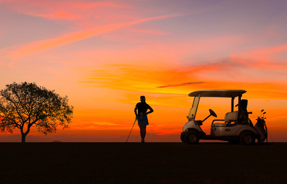 Woman professional golfer standing on golf course near golf cart with sun sky background