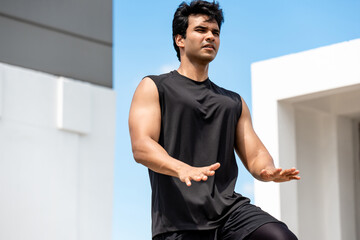 Handsome Indian man doing high knee tap exercise outdoors on building rooftop, open air home...