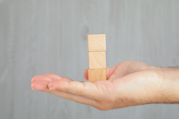 Business concept on grey background side view. hand holding tower of wooden cubes.