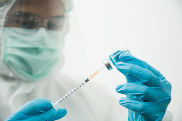 Doctor in ppe suit uniform wearing face mask protection virus holding medicine liquid vaccine vial bottle and syringe. COVID-19 concept.