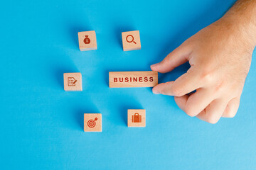 Business concept with icons on wooden cubes on blue background flat lay. hand holding wooden block.