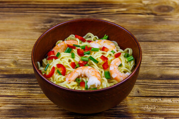 Bowl of instant Chinese noodles with shrimps, green onion and red hot chilli peppers on wooden table