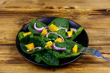 Tasty salad with spinach, orange, red onion and sesame seeds on wooden table. Healthy food or vegetarian concept