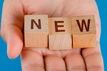 Business idea concept on blue background close-up. hand holding wooden cubes with word new.