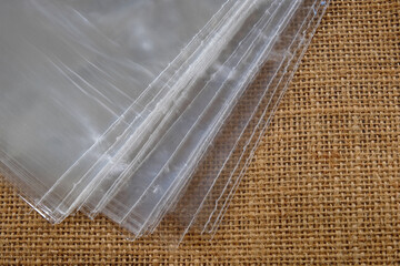 Sheets of clear plastic bag lying against a jute made shopping bag. Concept for plastic versus cloth bag, choosing between reusable bags vs throw away single use plastics. Closeup top view.