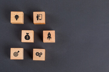 Business idea concept with icons on wooden cubes on dark grey background flat lay.