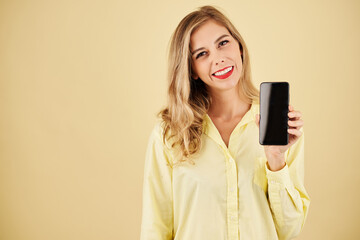 Fototapeta premium Studio portrait of cheerful blond woman showing new model of smartphone