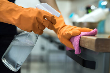 woman while cleaning the surface of a kitchen desk with sponge in her rubber gloves.