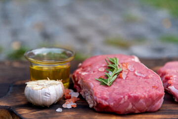 Raw meat beef steak organic fresh ingredient on wooden board table background in kitchen with rosemary, salt, garlic, tomato, black pepper, olive oil. Meat beef on wooden plate for beefsteak raw meat