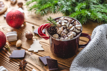 A cup of aromatic tasty hot chocolate with marshmallows decorated with red candy on a wooden table surrounded by Christmas accessories. Concept of a festive atmosphere and cozy New Year mood