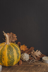 Pumpkin, tea, candles, cinnamon, yarn and fallen leaves on a wooden black background. Thanksgiving background. Vertically.
