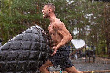 Close up portrait of a man flipping a tire. Hard workout on a rainy day.