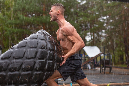 Close Up Portrait Of A Man Flipping A Tire. Hard Workout On A Rainy Day.