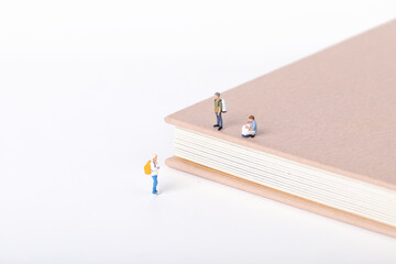 View of little figurines of students standing on and around a textbook on white background