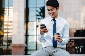 Smiling Young Asian Businessman Using Mobile Phone in the City